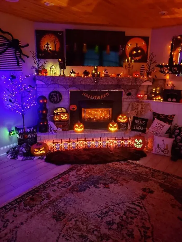 Cozy living room fireplace filled with glowing jack-o-lanterns and Halloween decorations.