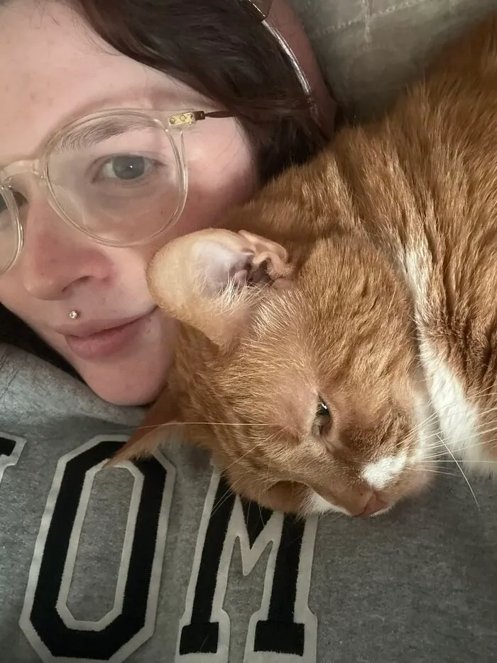 A woman with glasses close to her orange tabby cat, showcasing a pet's life story.
