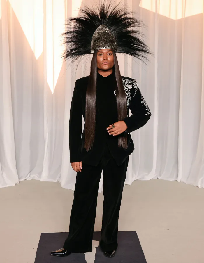 Celebrity wearing a black suit with an elaborate feathered headpiece at the Academy Museum Gala