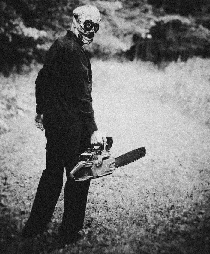 A masked figure standing in a field holding a chainsaw, scene from scarier Halloween stories.