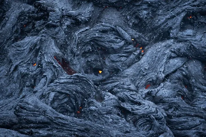 Dark, swirling lava texture with glowing red spots captured in natural landscape photography.