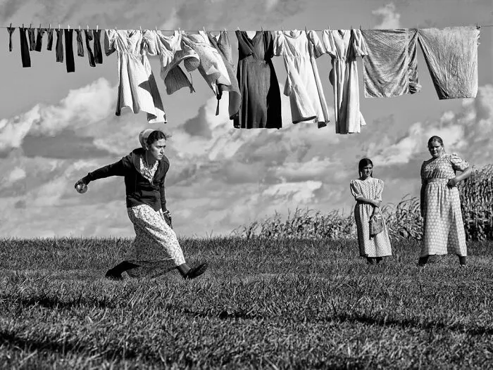 Monochrome scene of women in a field under hanging laundry, featured in Exposure One Awards.