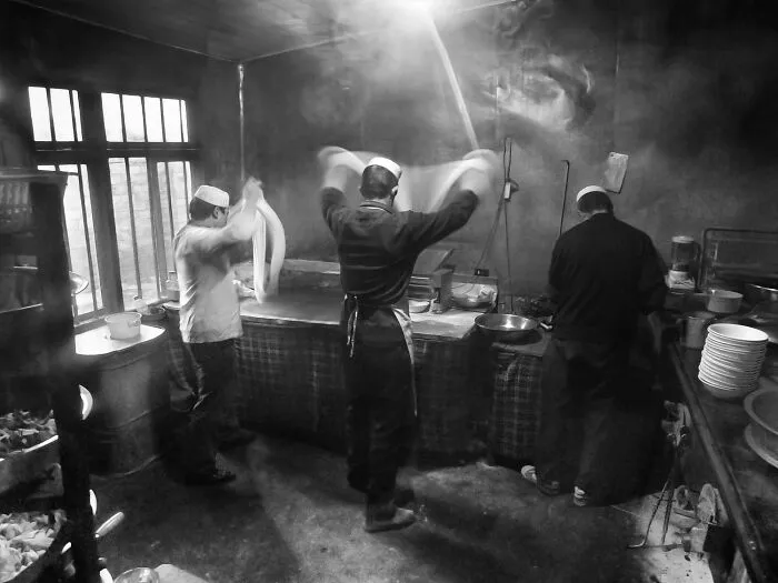 Documentary black-and-white photos of chefs making hand-pulled noodles in a traditional kitchen.