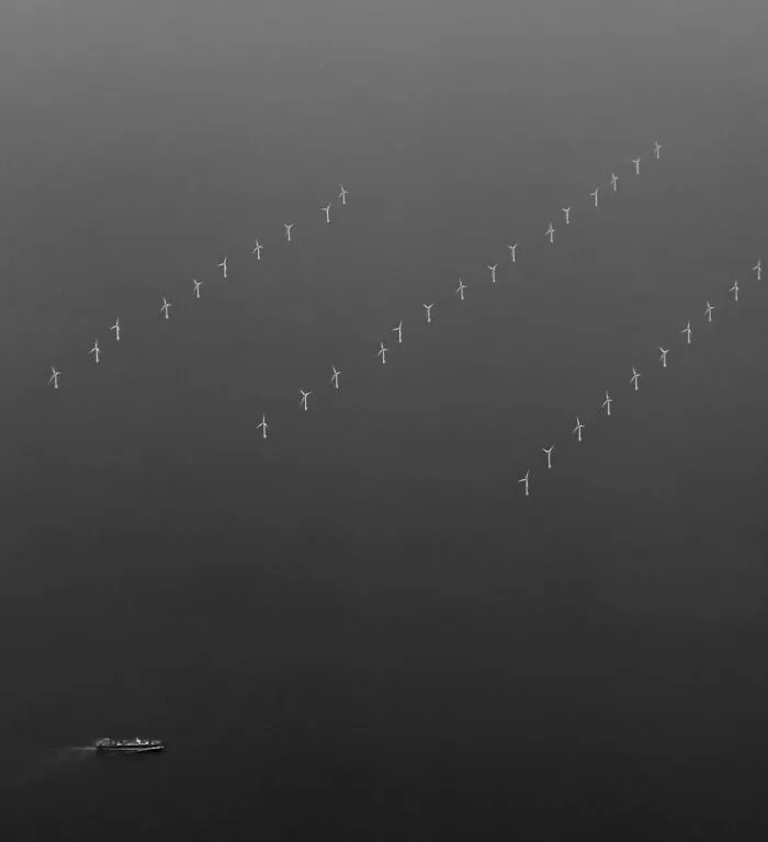 Minimalist aerial black-and-white photos of offshore wind turbines and a small boat on misty ocean waters.