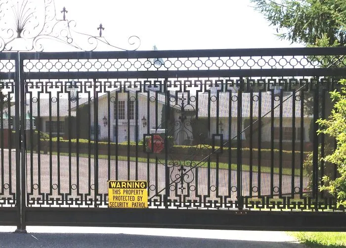 A closed security gate with a warning sign guarding a compound used by lesser-known cults.