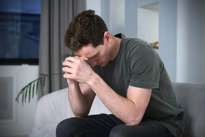 A distressed man sitting on a couch with hands on his forehead, reflecting on lifelong friendships lost.