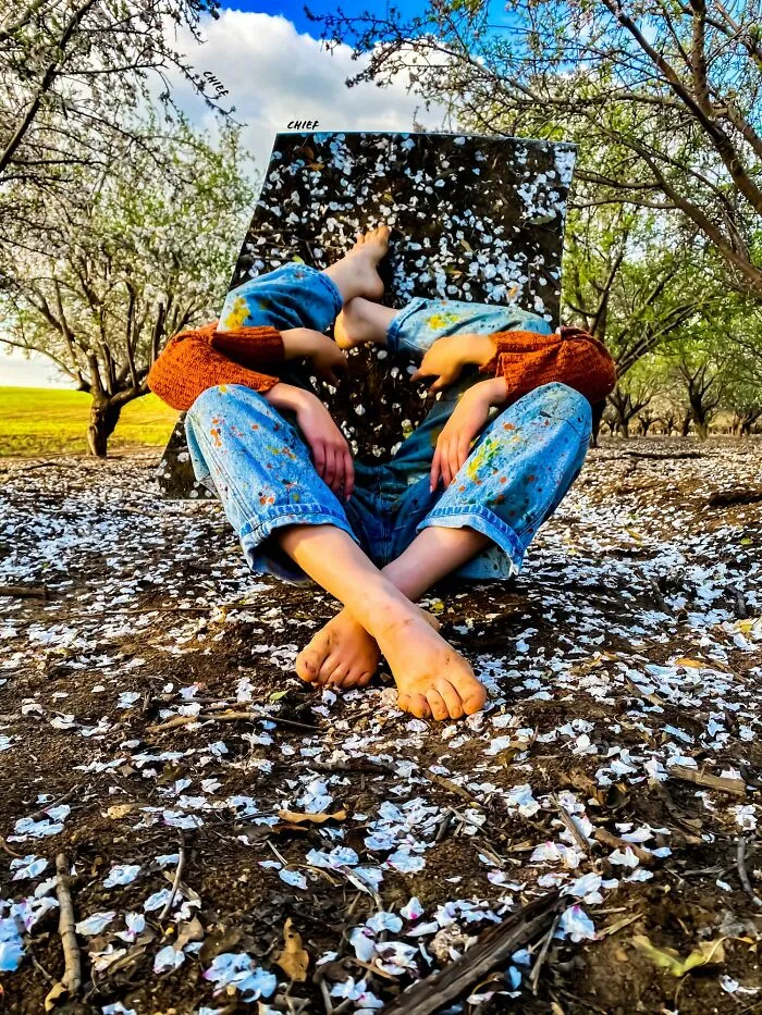 Person sitting in blossoming orchard with mirror capturing iPhone photo