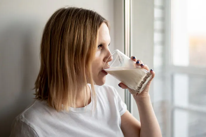Woman drinking glass of milk by window in humorous revenge story setting