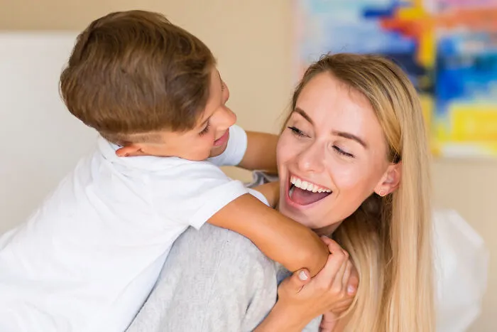 A happy young mother giving her small son a piggyback ride, showing signs of overprotective helicopter parenting.