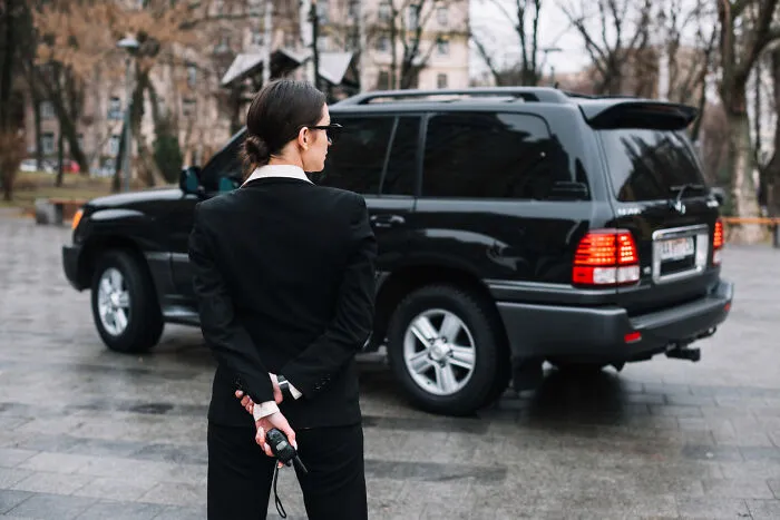 A security guard standing near a black SUV on a city street, relating to odd funeral stories.