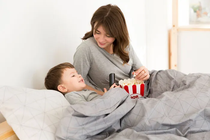A mother and her young son watching a movie in bed with popcorn, highlighting healthy family bonding