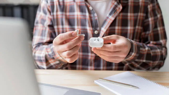 Hands holding wireless earbuds and charging case on desk