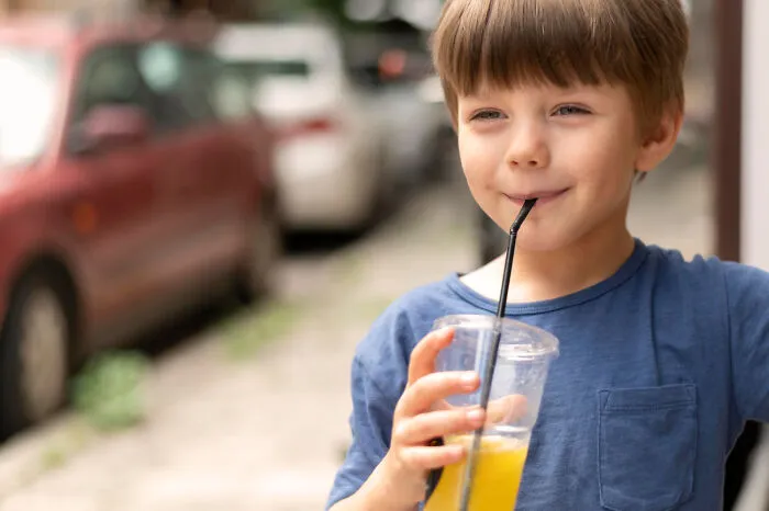 A young boy drinking juice through a straw, showing a moment of childhood without helicopter parenting