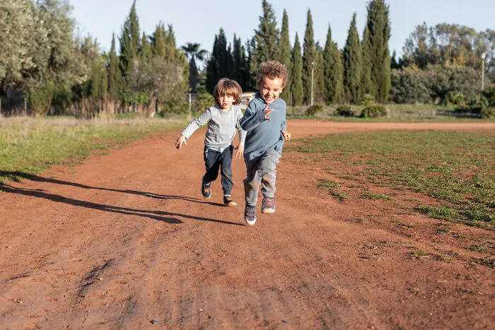 Two young kids running freely outdoors on a dirt path, demonstrating a contrast to helicopter parenting
