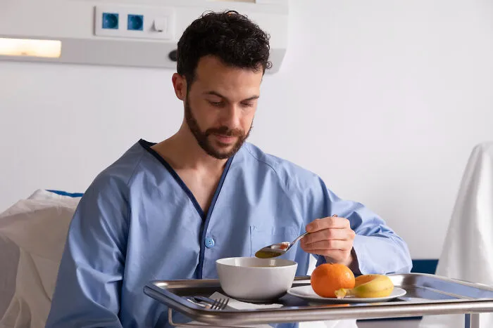 A healthcare worker's patient eating soup in a hospital bed with a fruit tray.