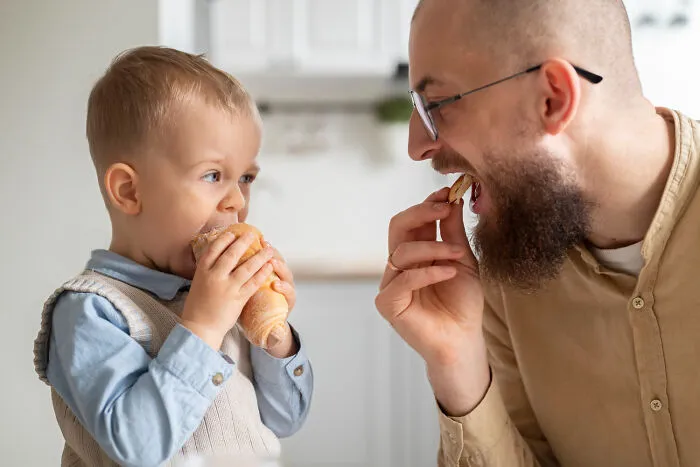 Father feeding a snack to his son, showing helicopter parenting over-involvement in daily choices.