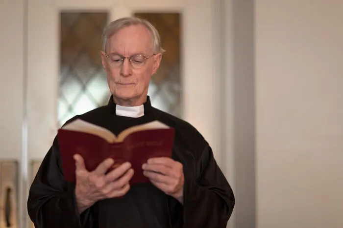 A priest reading from a red Bible, representing moments when things went wrong at funerals.