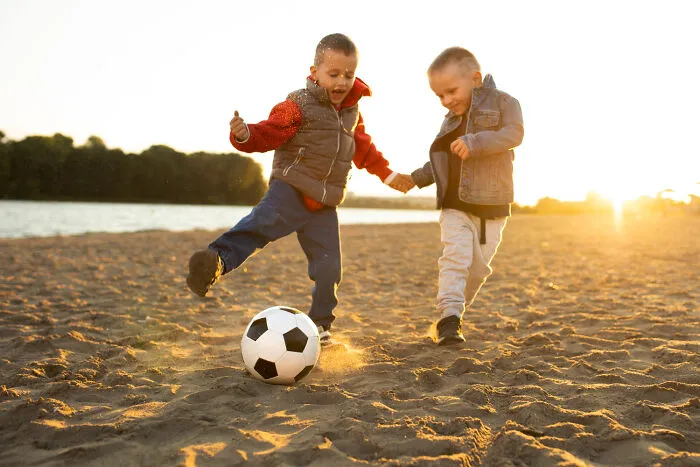 Two young kids playing soccer on a beach, illustrating freedom from helicopter parenting