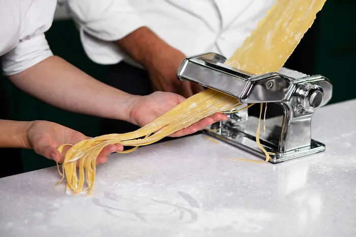 Hands making fresh pasta with a pasta machine