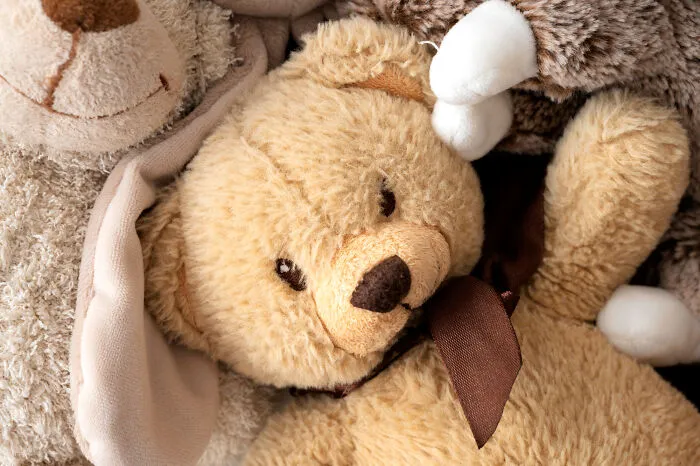 A plush teddy bear among stuffed toys representing funny moments at funerals.