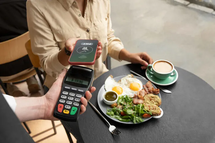 A person using a smartphone to pay at a restaurant table, representing dating expenses and a second date