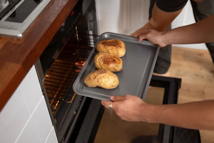 Person placing baked potatoes on tray into oven for cooking in funny revenge ideas