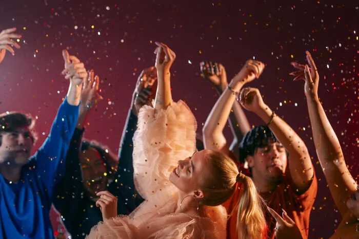 Excited group of friends dancing and celebrating under falling confetti.