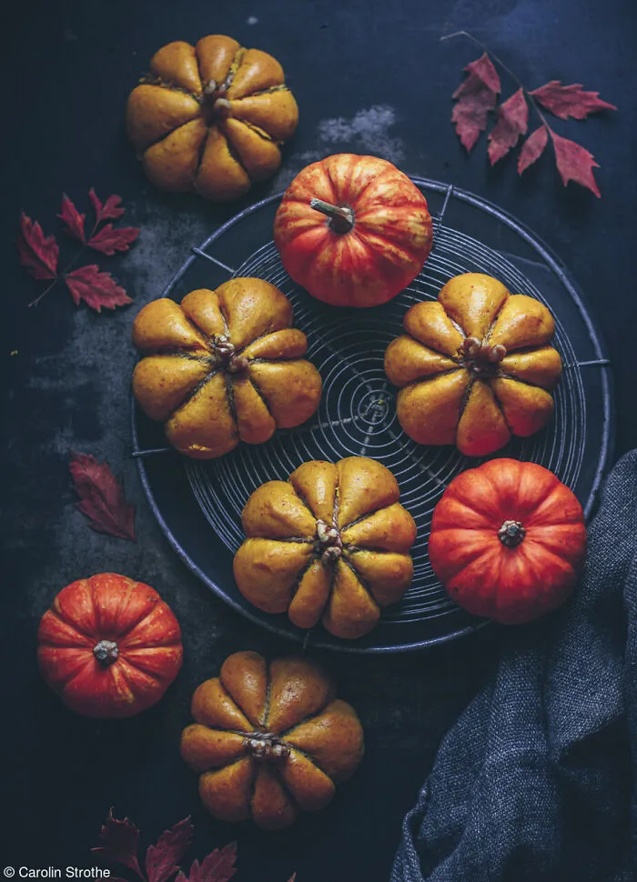 Artistic arrangement of mini pumpkin rolls and small real pumpkins served on a round wire rack.
