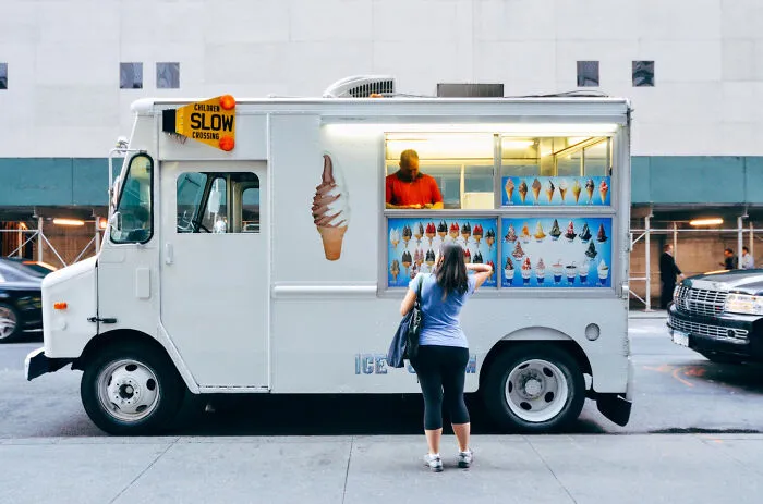 A woman buying ice cream from a white food truck outdoors, relevant to funny moments at funerals.
