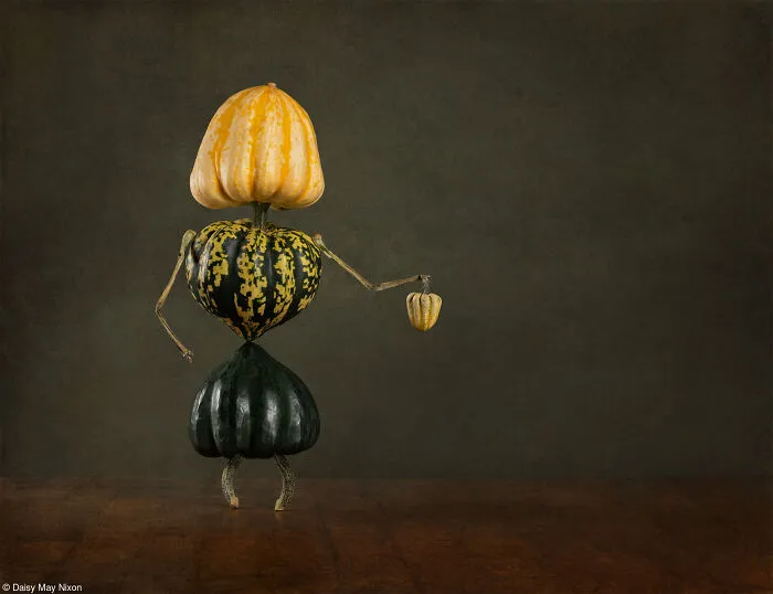 Whimsical human figure skillfully crafted from stacked gourds and pumpkins on a dark background.
