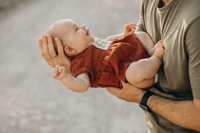 An adult carefully holding a happy baby outdoors, highlighting unexpected occurrences at funerals.