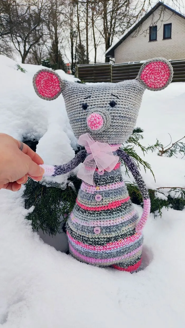 A mouse crochet creature with pink ears standing in the snow.