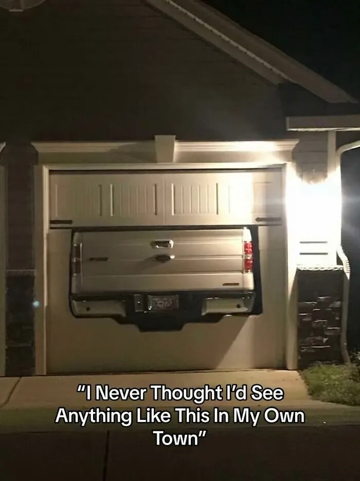 Truck bed oddly sticking through a custom cutout in a closed white garage door, showing a home renovation fiasco.