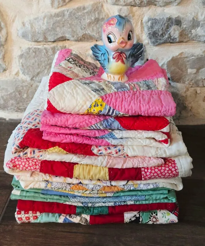 Stack of colorful vintage quilts with ceramic bird thrift store fabric