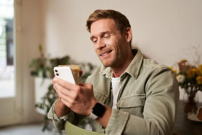 A man smiling while looking at his smartphone over coffee, considering whether to schedule a second date
