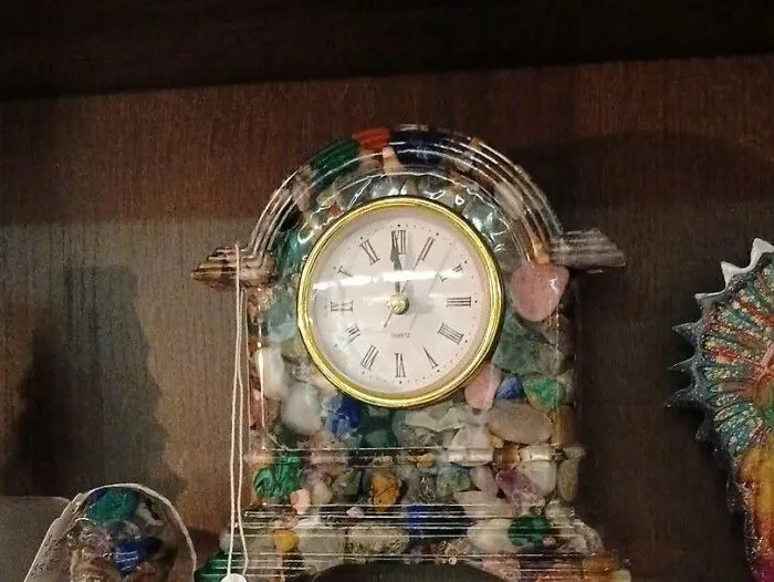 A unique table clock embellished with colorful mosaic polished stones, an interesting thrift find sitting on a wooden shelf.
