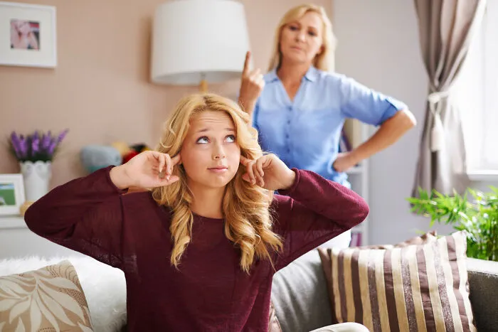 A teenage girl covering her ears while her mother lectures her, demonstrating stressful helicopter parenting.
