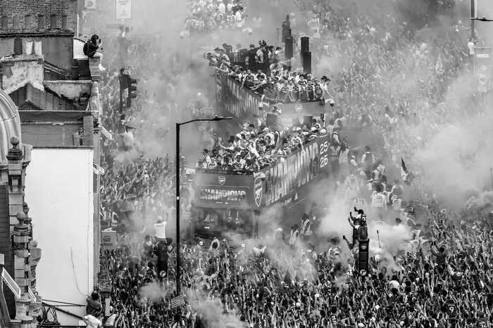 A black-and-white photo of a crowded street parade with championship buses from Exposure One Awards.