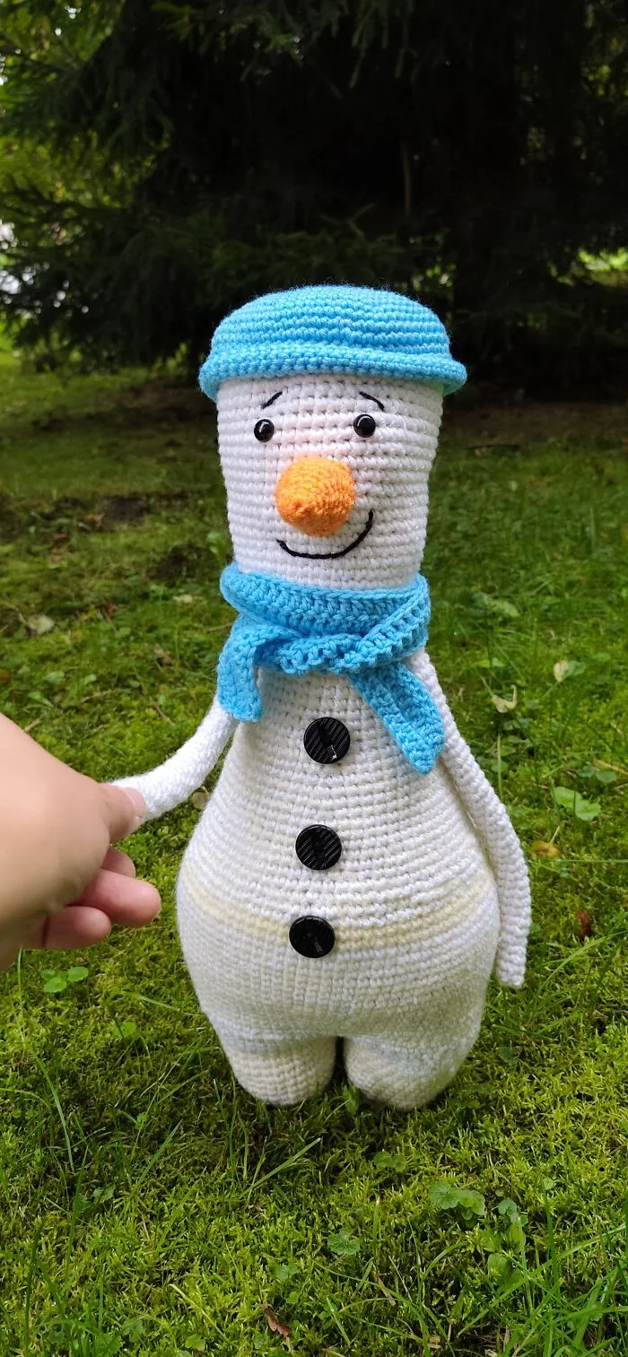 An adorable snowman crochet creature wearing a blue hat and scarf.