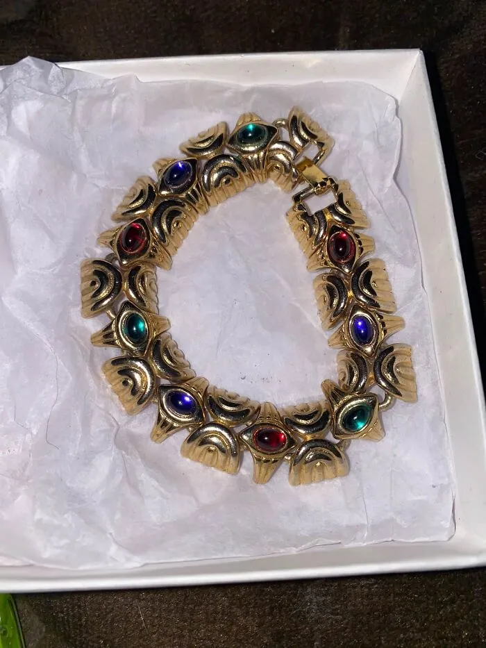A vintage gold bracelet with colorful faux jewels displayed in a white jewelry box, a stylish thrift find.