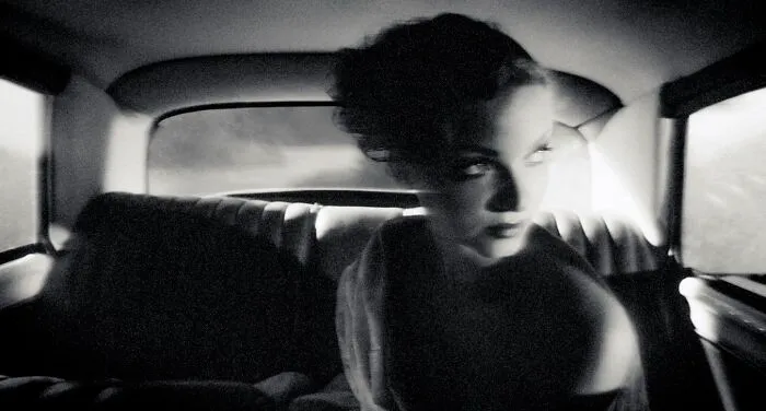 Dramatic black-and-white photo of a woman looking out from the back seat of a classic vintage car.