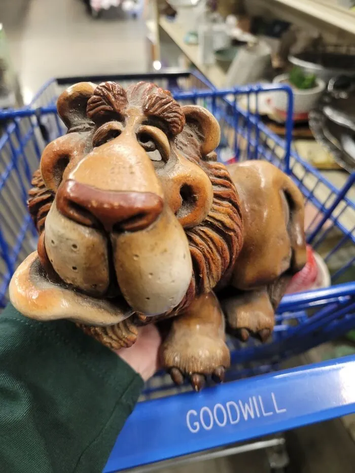 A quirky clay lion figurine resting inside a blue shopping cart, a unique thrift find.