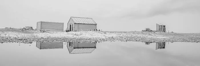 Black-and-white photos of wooden huts reflecting in a calm water pool