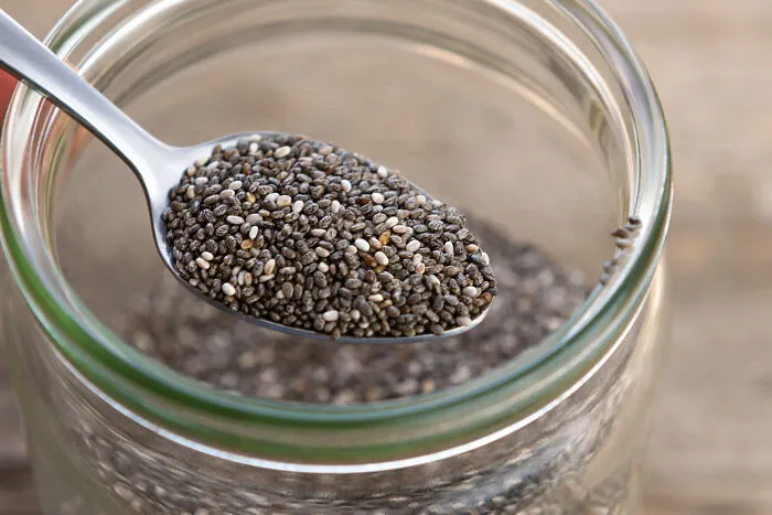 Spoonful of chia seeds over glass jar filled with seeds
