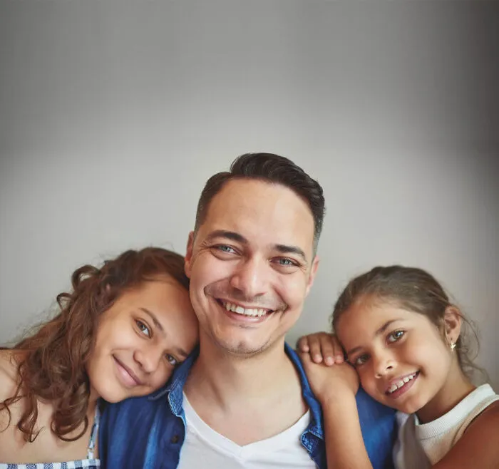 A smiling father sitting closely with his two daughters, associated with family events and funerals.