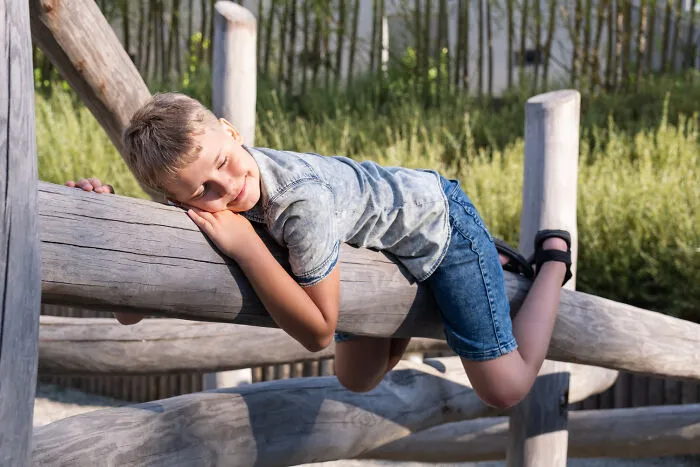 Young boy playing freely on logs, away from helicopter parenting control