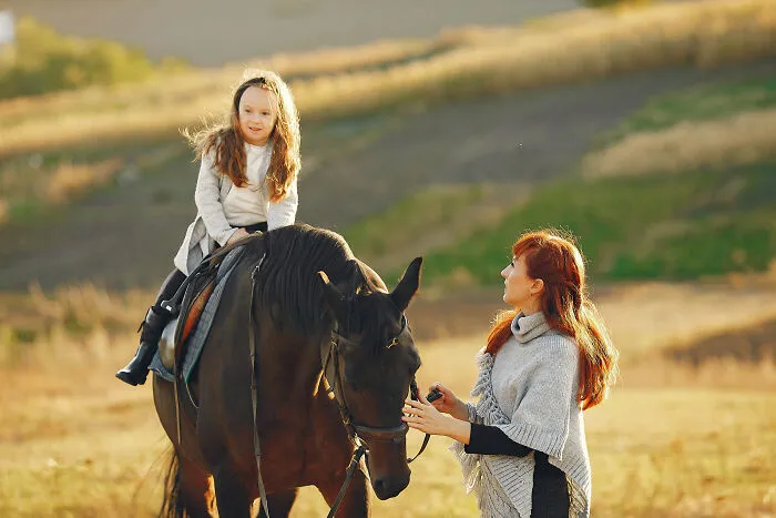 Child riding a horse with adult supervisor in outdoor horse riding scene