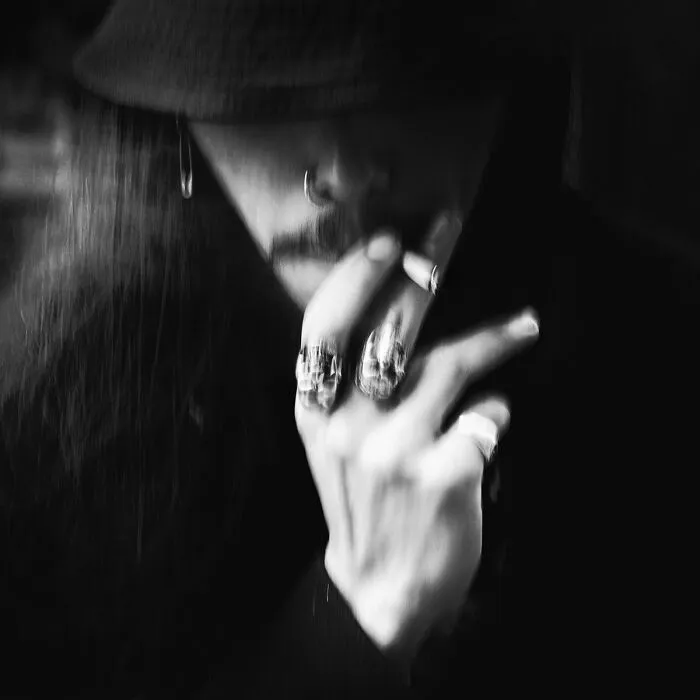 Moody black-and-white photo of a person wearing a bucket hat, smoking a cigarette, and displaying rings.