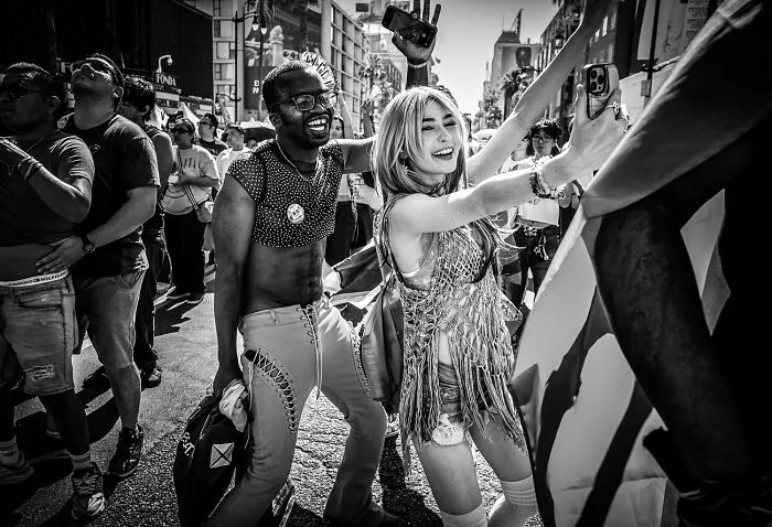 Lively black-and-white photo of smiling people taking a selfie at an outdoor street parade.