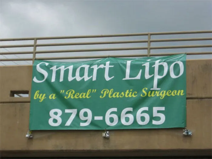 A green outdoor banner with misused quotation marks around the word real in real plastic surgeon.